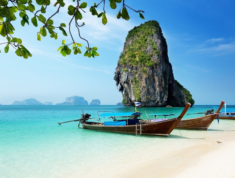 Plajă cu bărci tradiționale și o stâncă uriașă în Thailanda
